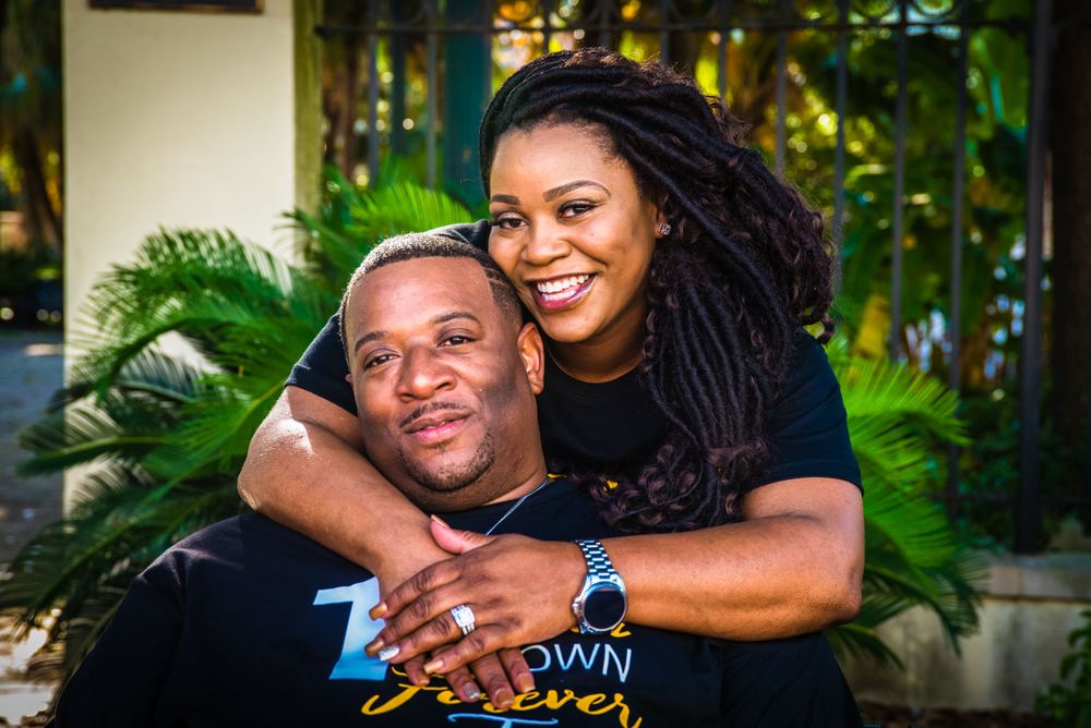 Couple sharing a warm embrace outdoors with palm trees in background.