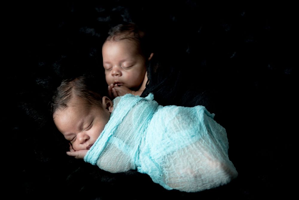 A sleeping newborn in light blue clothing photographed on a black background.