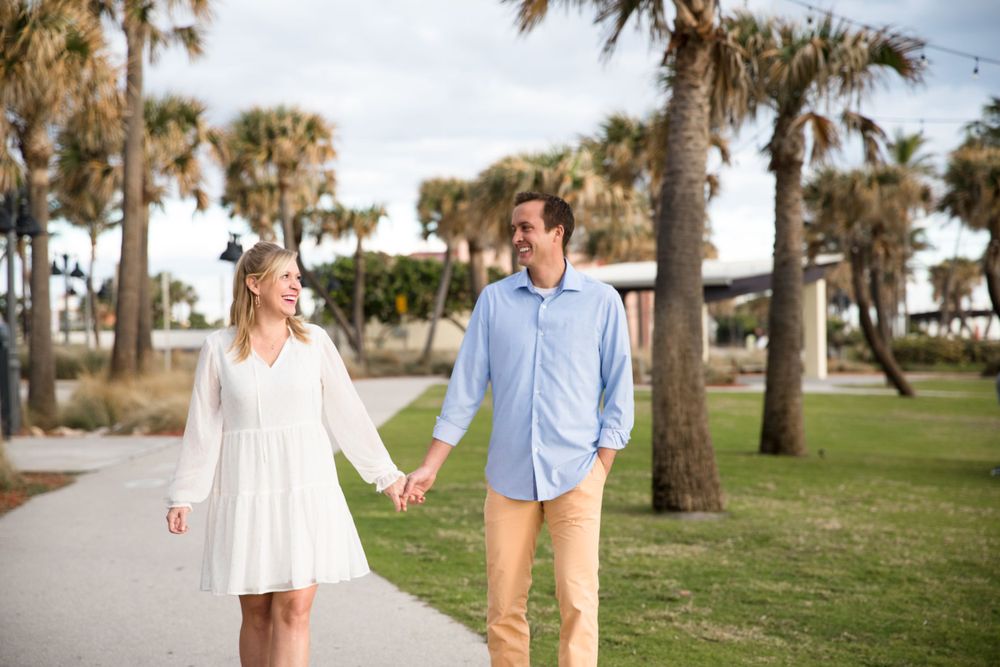 Romantic couple strolling hand in hand along palm tree lined beachside path.