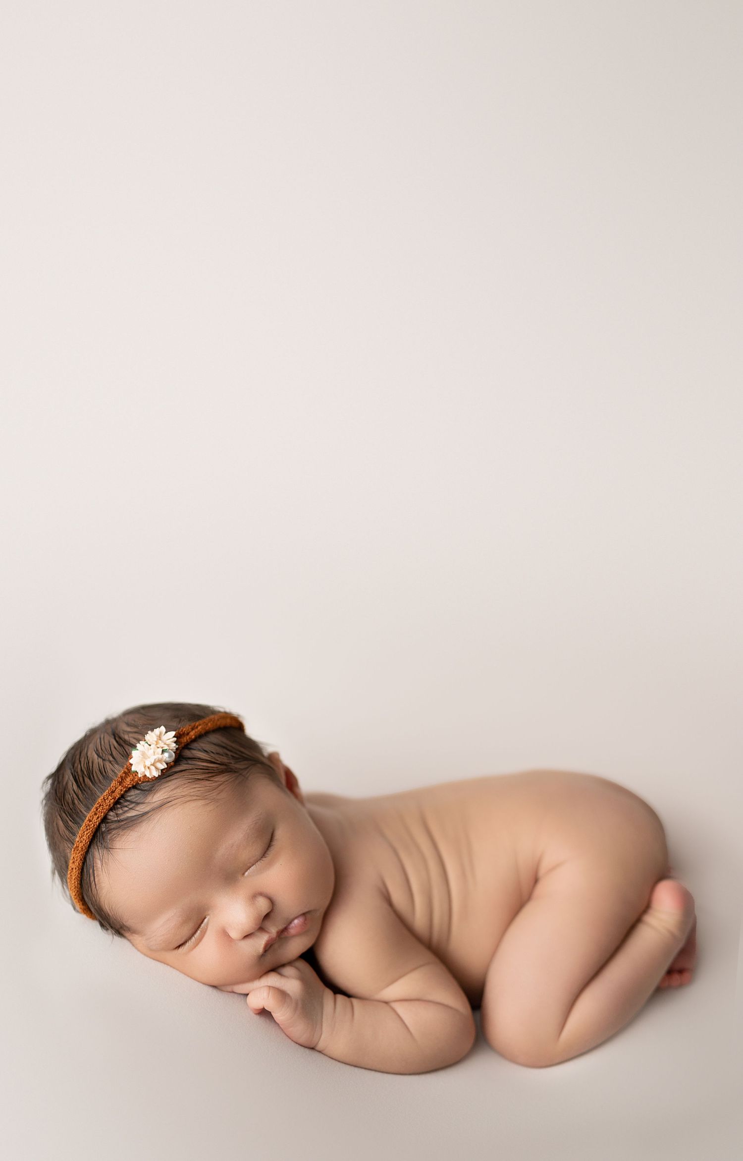 Artistic series of newborn baby sleeping on white backdrop with delicate hair accessory.