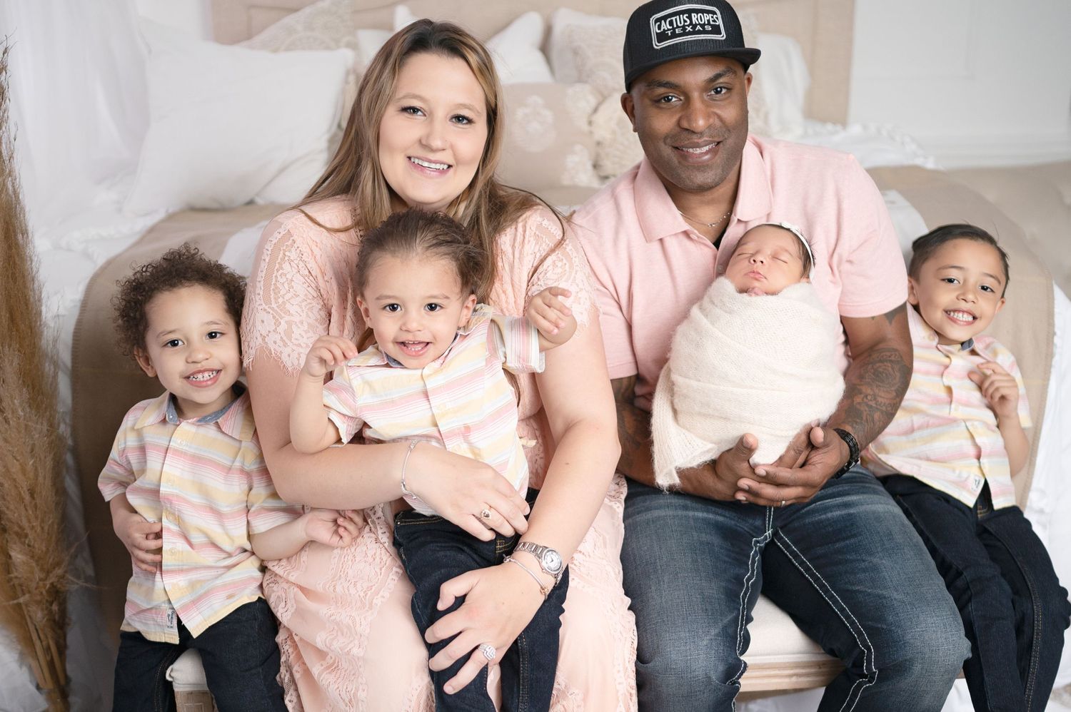 Happy family wearing coordinated pink and beige outfits sitting together on white backdrop.