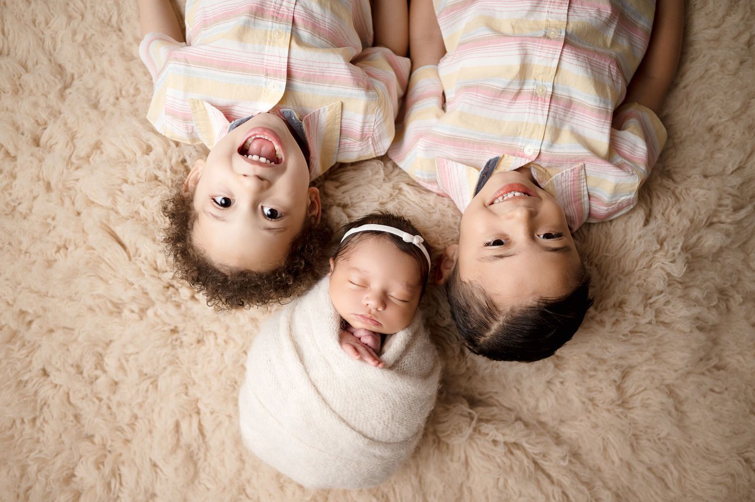 Three children in matching outfits lying on beige carpet smiling at camera.