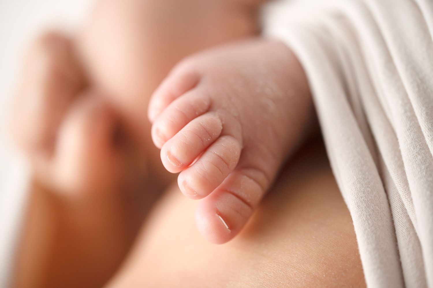 Close-up of tiny newborn baby feet against white fabric background.