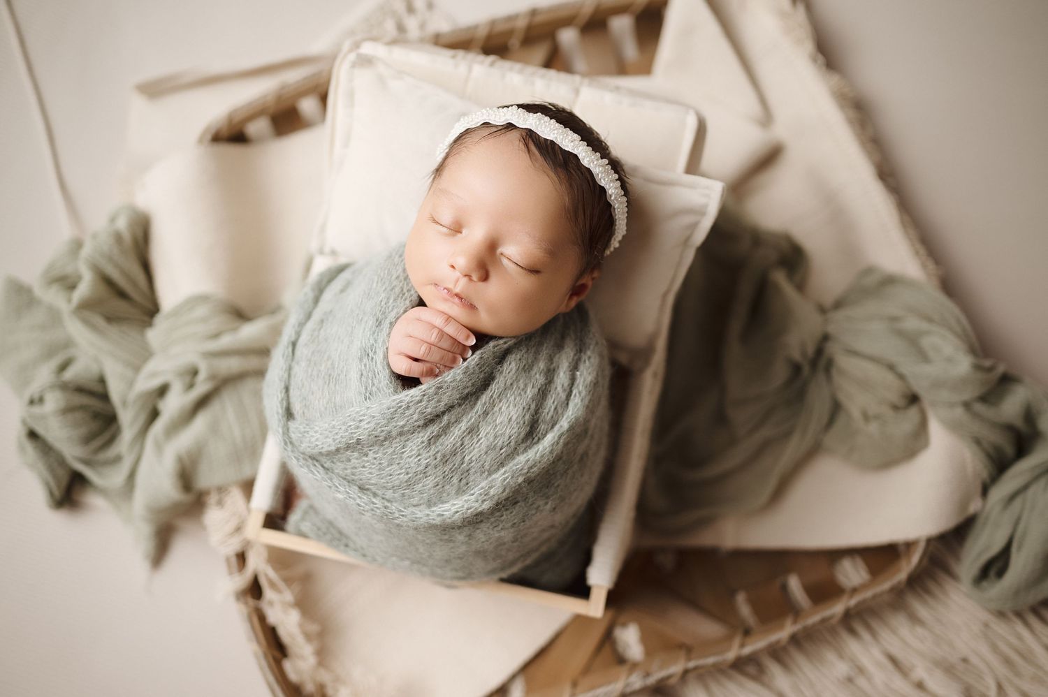 Sleeping newborn wrapped in gray swaddle lying in wooden prop basket with neutral tones.