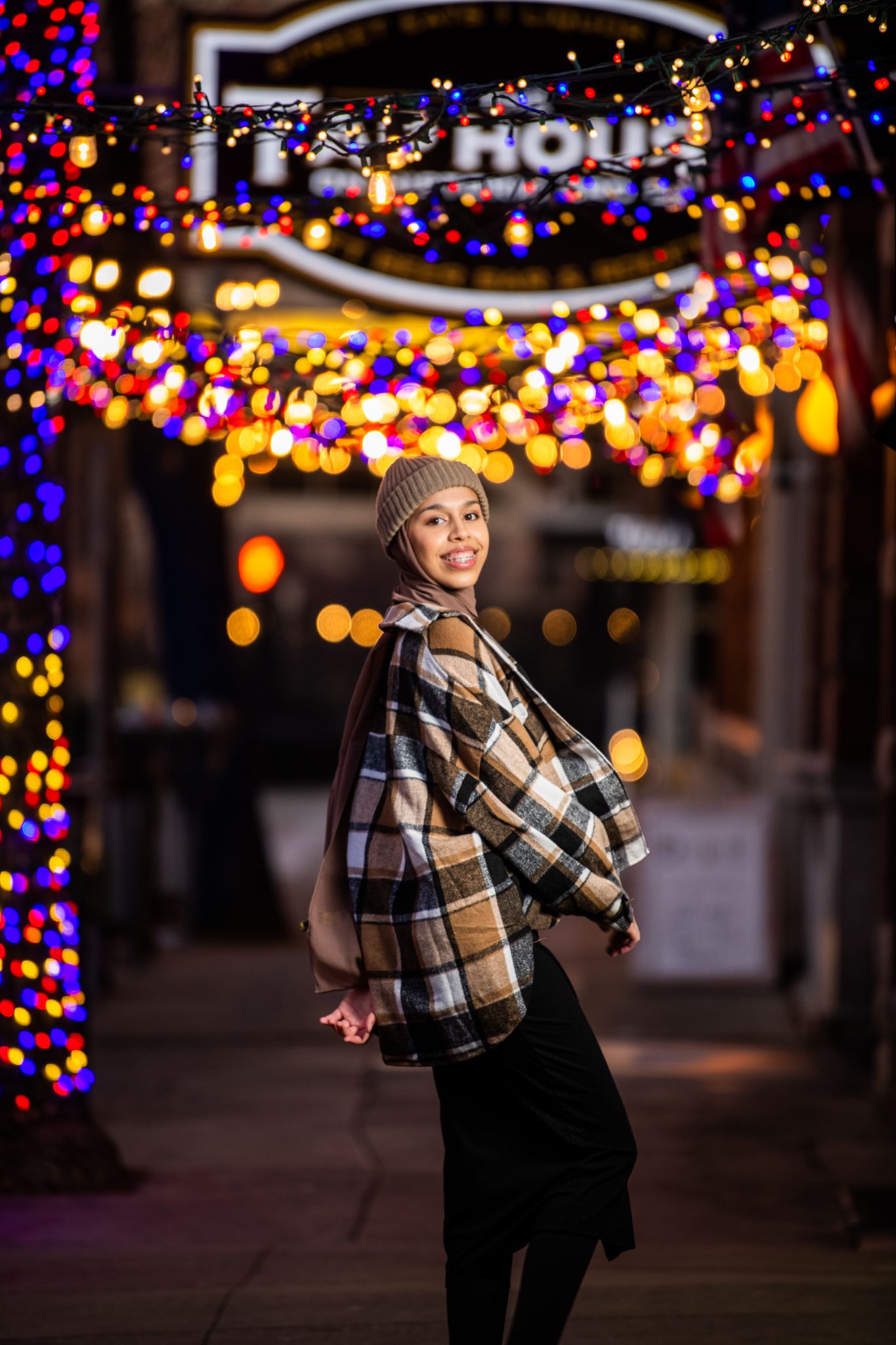 High school senior girl posing at night with lights twinkling in the backgroundd