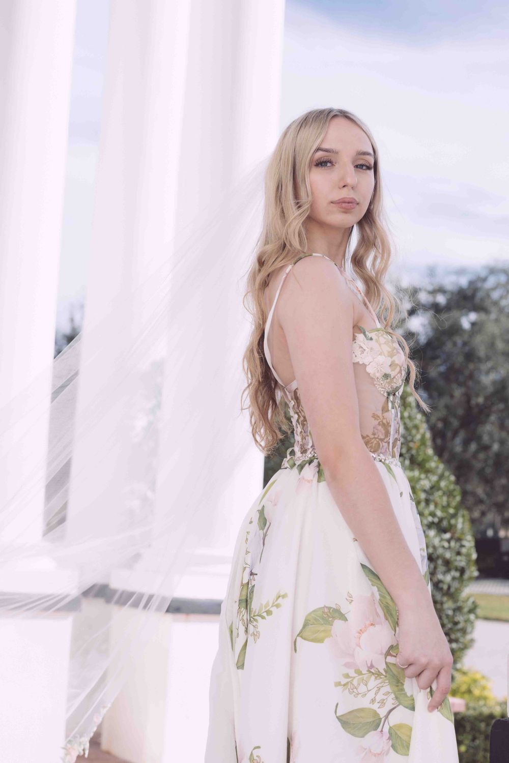 A floral print wedding gown with illusion details photographed against white columns.