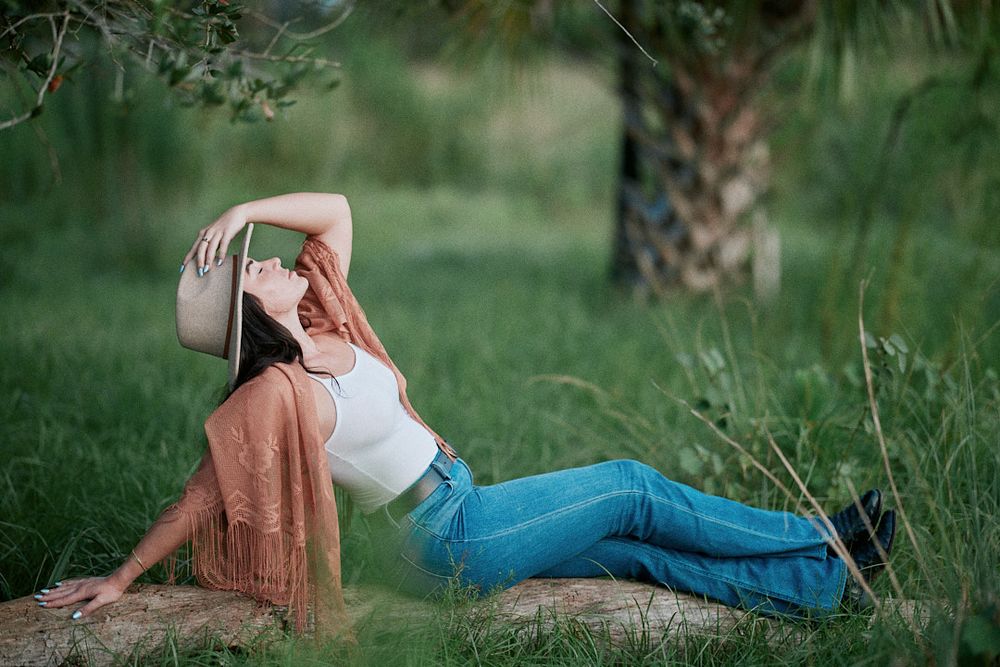 Relaxed outdoor portrait with western-inspired styling on grassy backdrop.