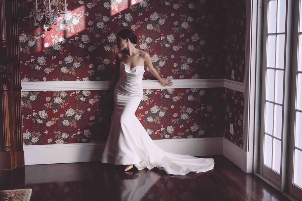 Wedding dress showcase in front of vintage floral wallpaper with dramatic lighting.