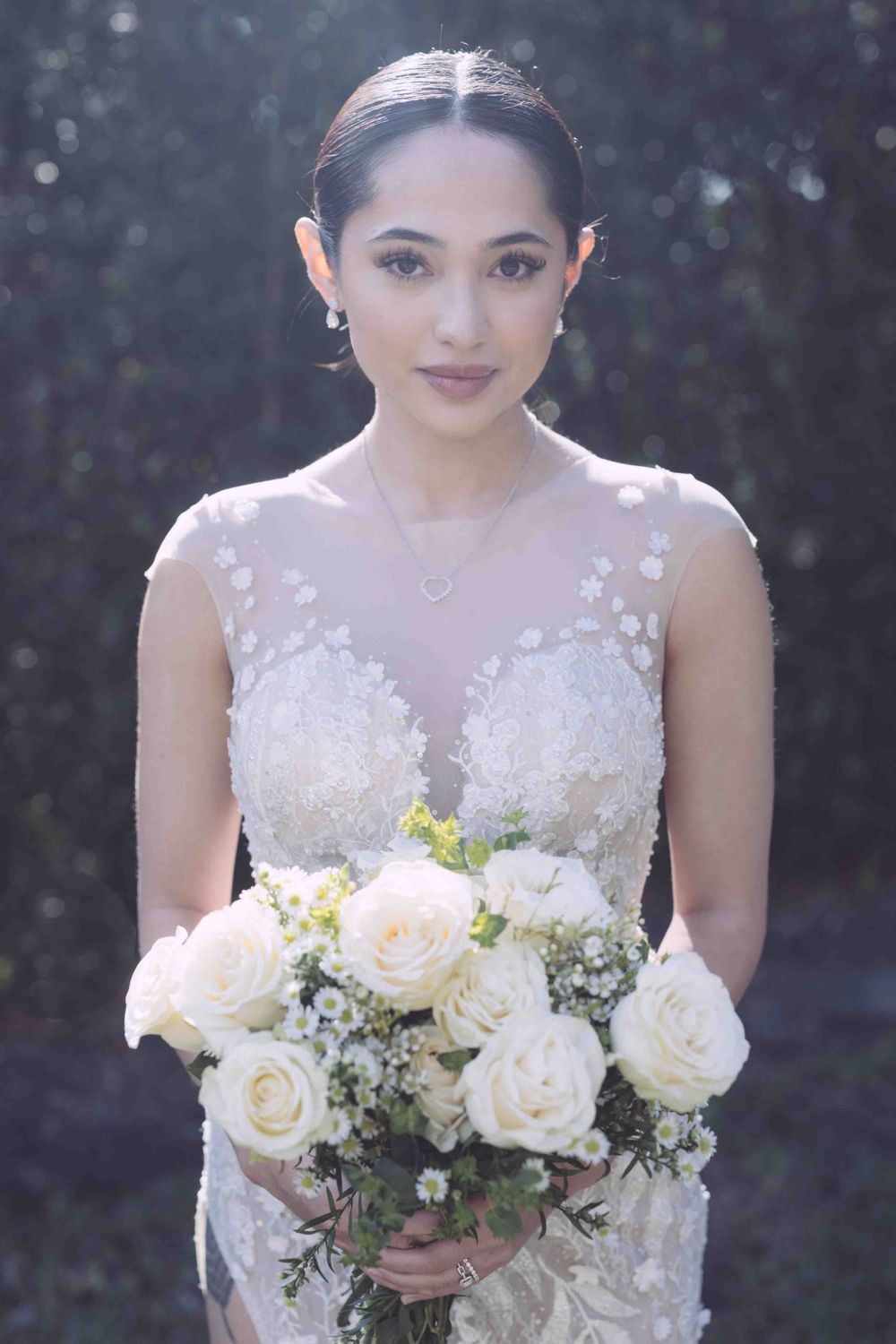 A bride holds a classic white rose and baby's breath bouquet in delicate lace gown.
