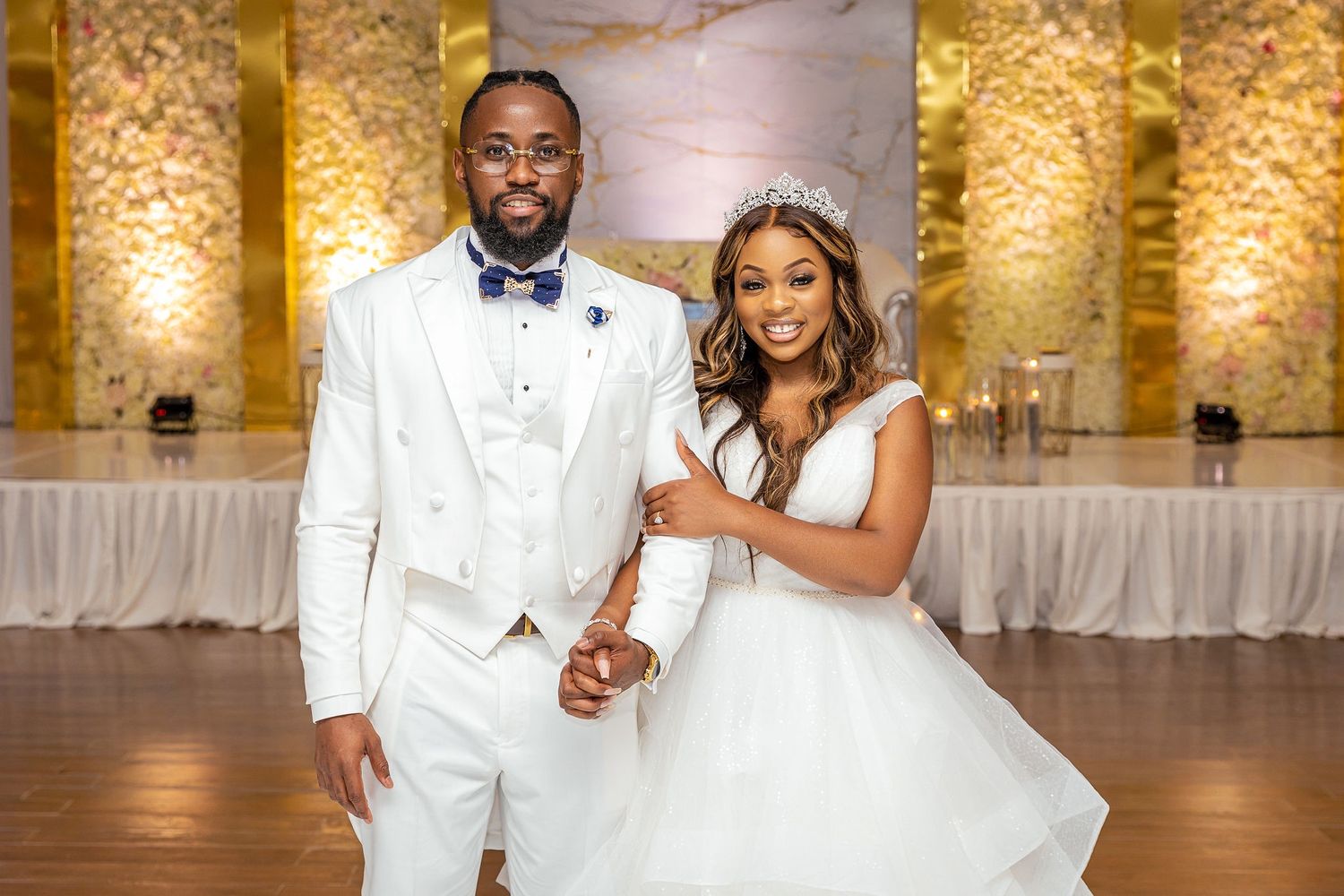 Bride and groom in white attire pose together in an elegant event space.