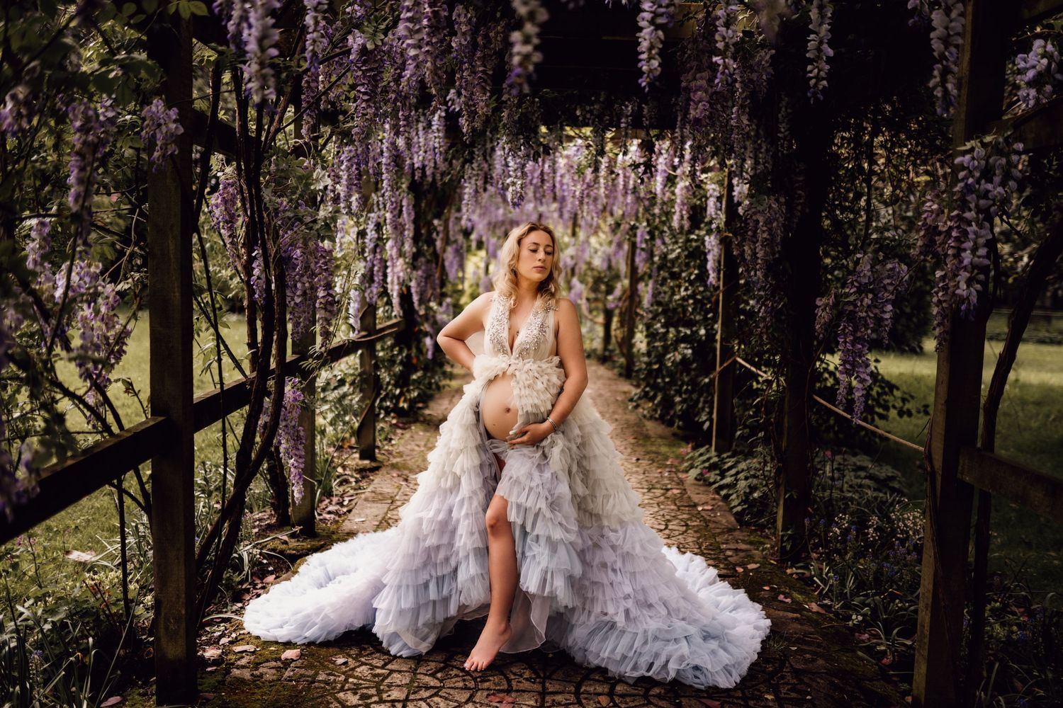 Enchanting maternity portrait under hanging wisteria with dramatic ruffled gown.