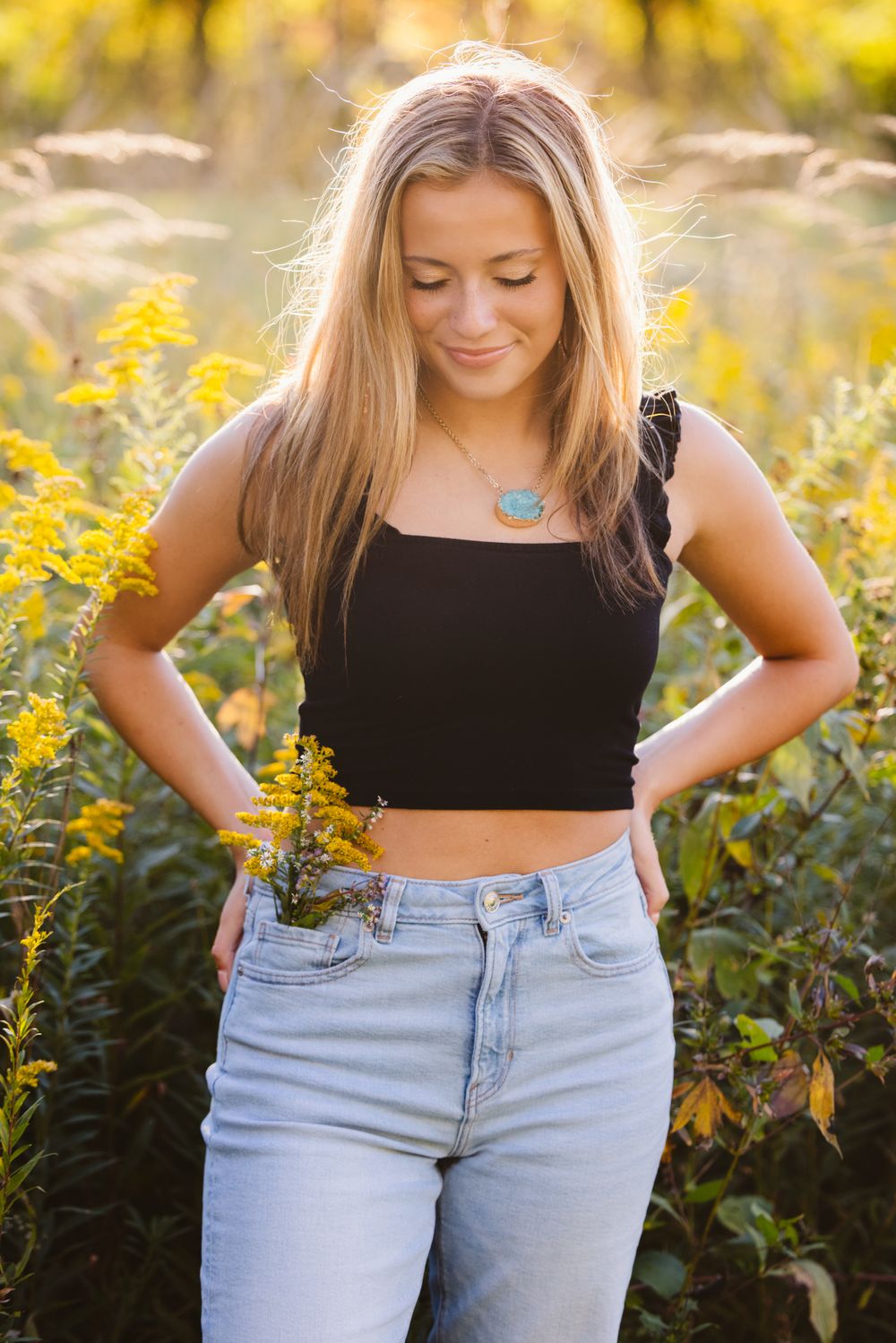 Portrait in golden wildflower field wearing black crop top and light denim jeans.