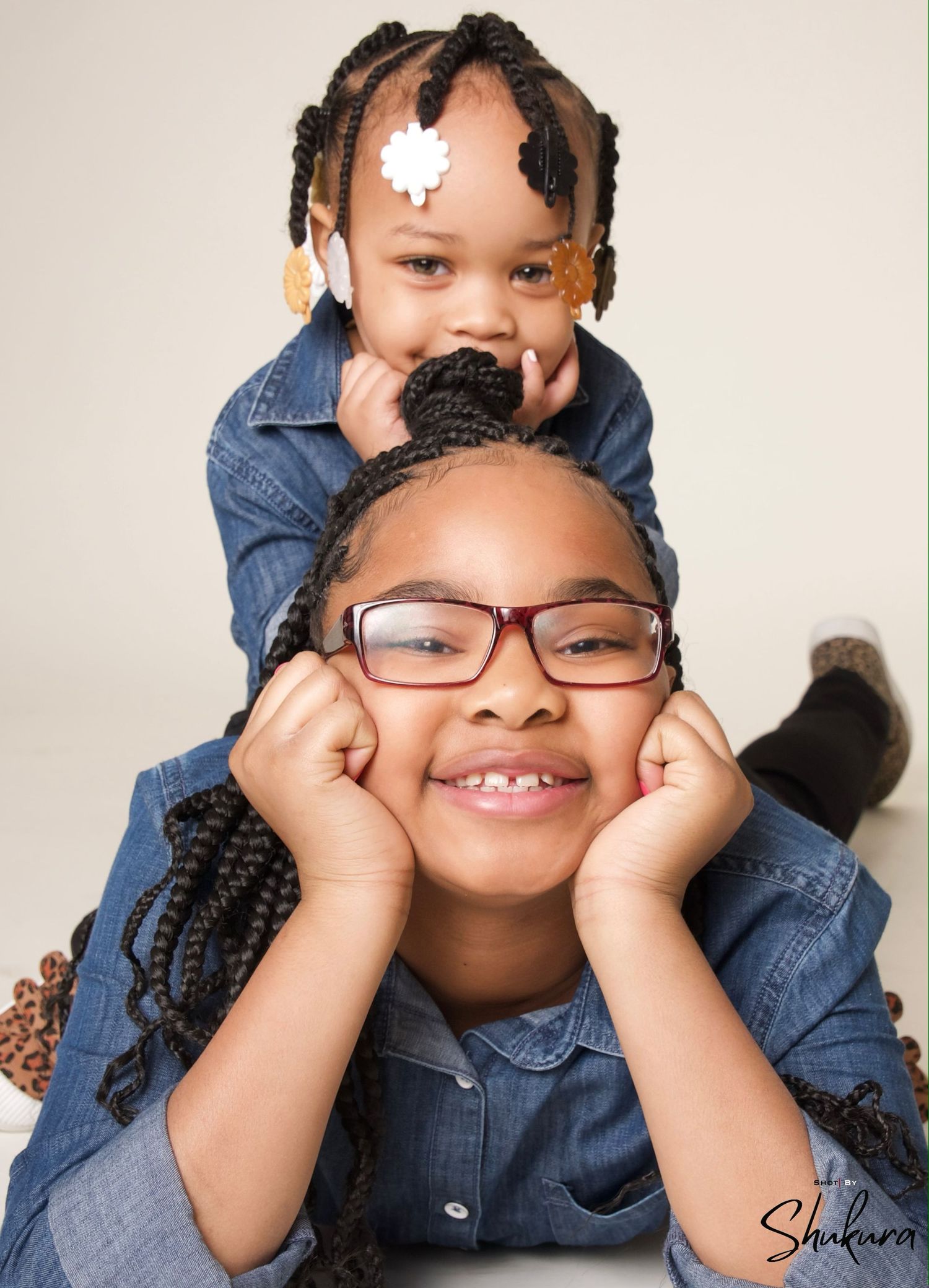 Two children in denim shirts posing playfully for a portrait against white background.