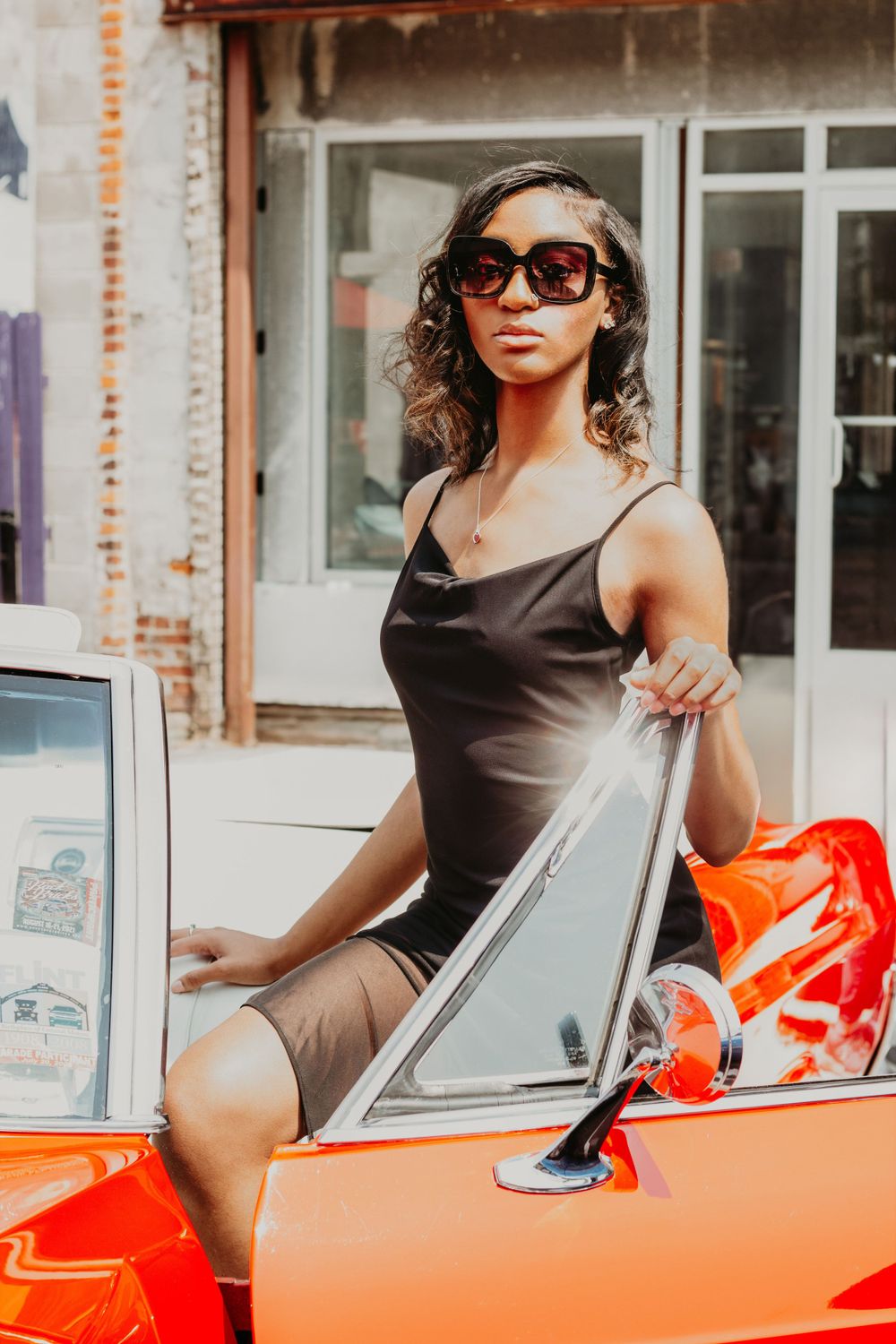 Woman in dark dress and sunglasses posing with bright red vintage car.