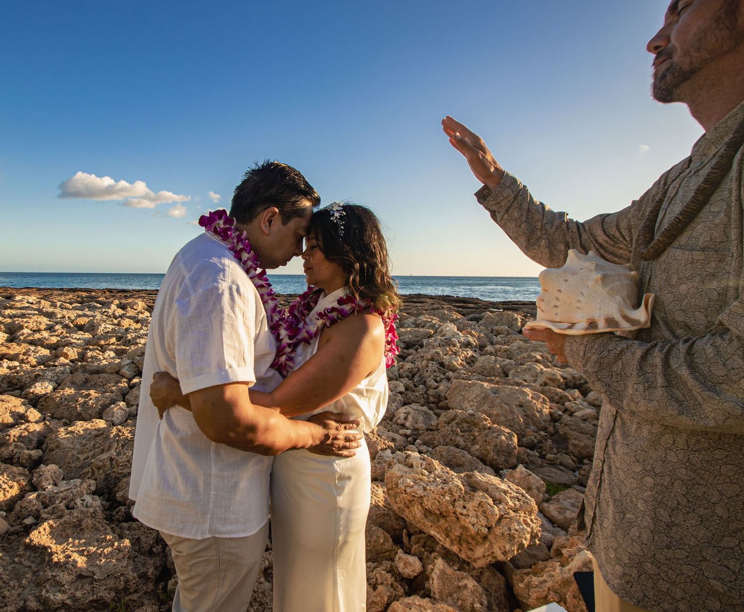 Oceanside wedding ceremony on volcanic rocks with waves crashing in background.