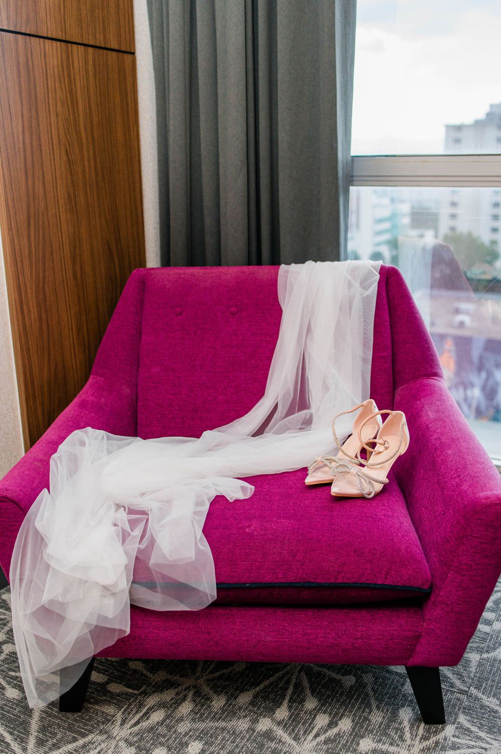 wedding veil laying on pink chair alongside wedding shoes