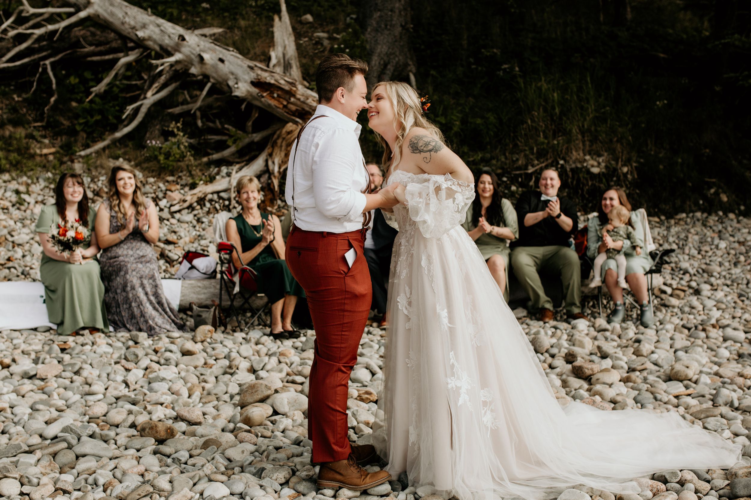 Wedding ceremony on a rocky beach with guests watching the celebration.