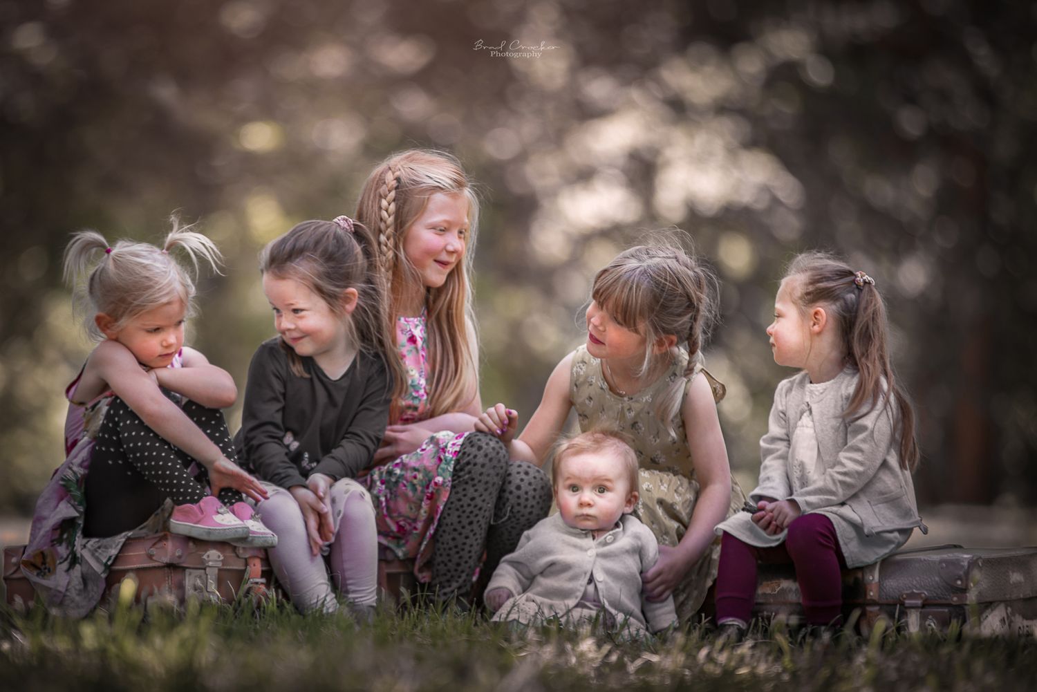 A group of children sitting together on the ground in a dreamy outdoor setting with soft bokeh lighting.