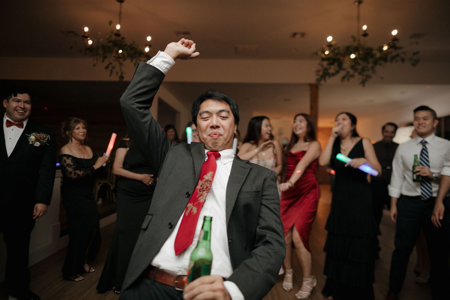Party guest in formal attire dancing energetically at an indoor celebration.