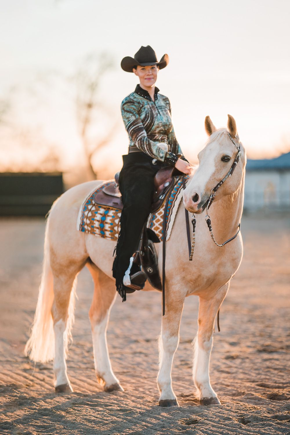 Porträttbild på kvinna som rider sin häst hon har på sig en cowboyhatt och solen lyser mjukt
