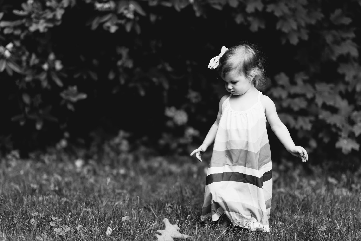 A black and white photo of a small child in a white dress walking in a grassy field.