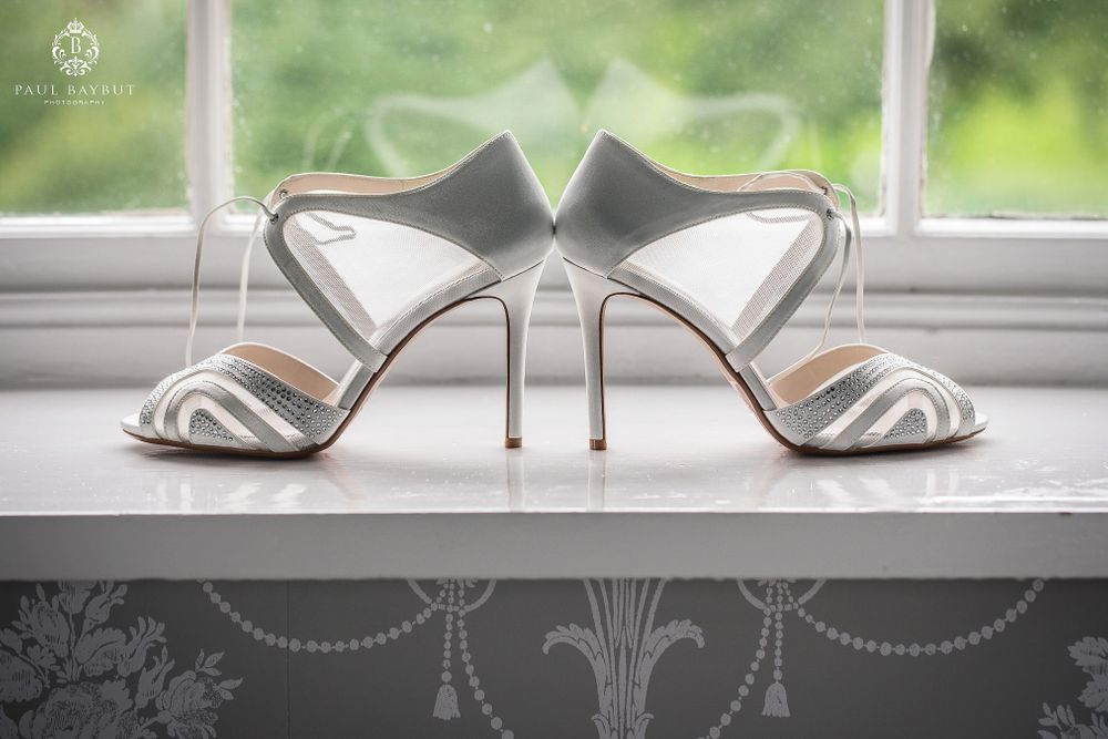 Elegant silver wedding shoes with stiletto heels displayed on a windowsill.