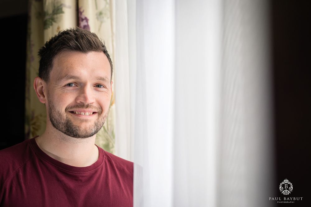 Portrait of a person in burgundy shirt standing by a bright window.