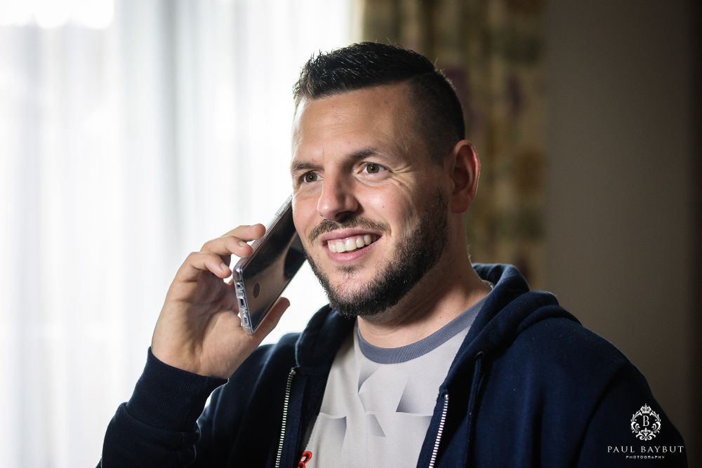Person in navy hoodie smiling while talking on phone near window.