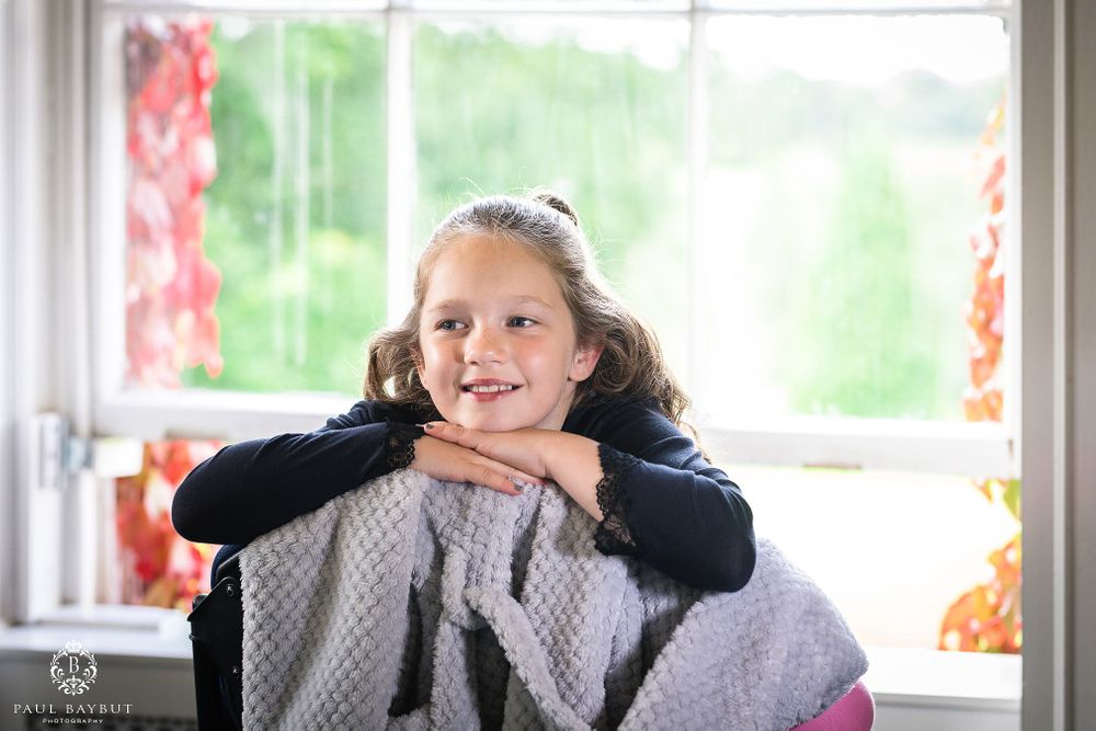 Young person resting chin on hands by window with red curtains.