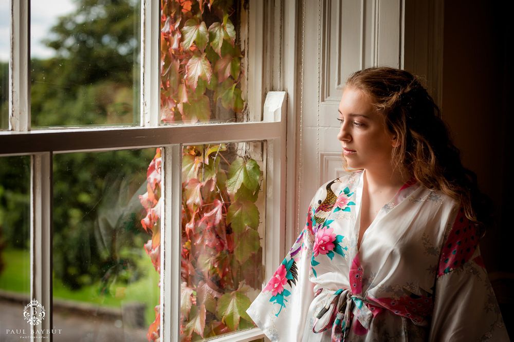 Person in floral robe gazing thoughtfully out window with autumn leaves.