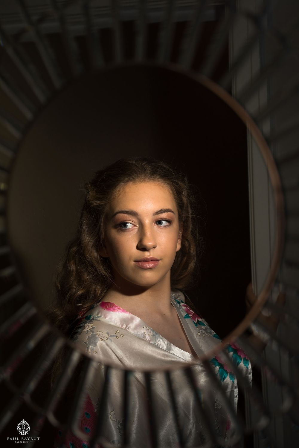 Dramatic portrait in silk robe reflected in circular mirror with moody lighting.