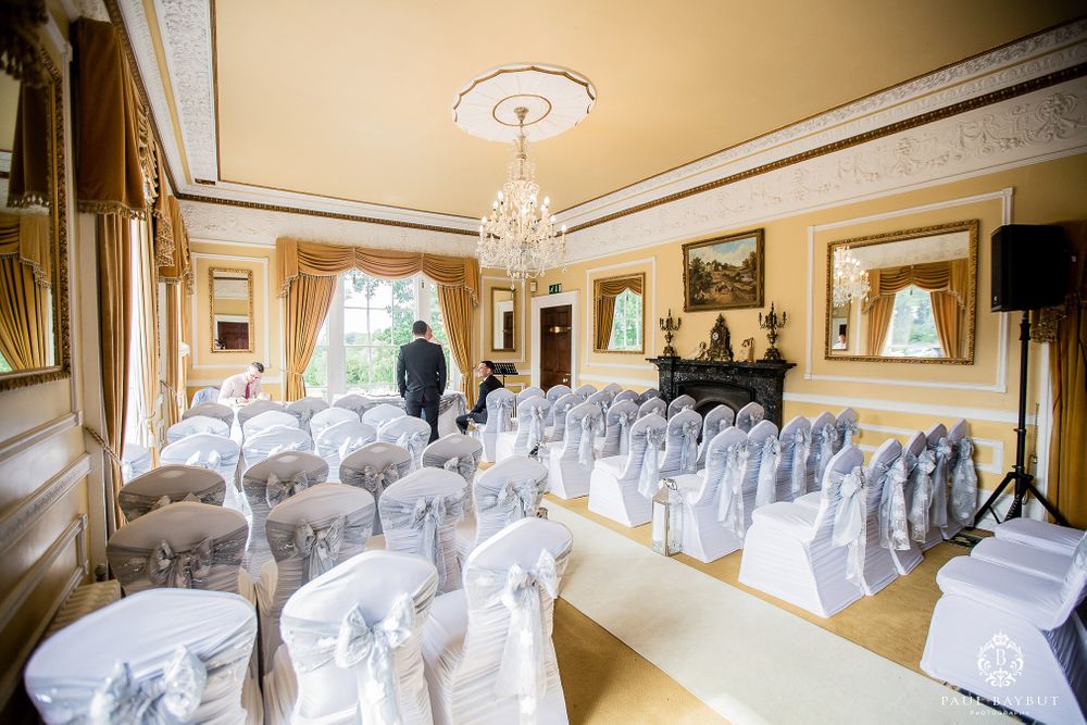 Elegant wedding ceremony room setup with white chairs adorned with silver sashes and crystal chandelier.