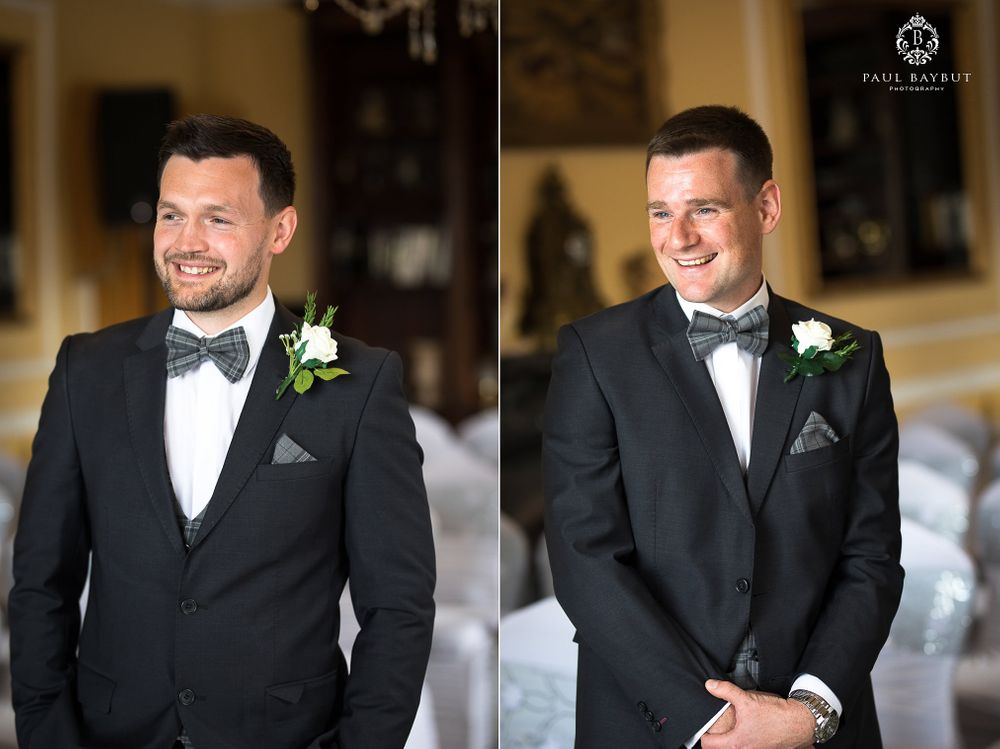 Two groomsmen in matching black tuxedos and bow ties smile during a formal wedding ceremony.