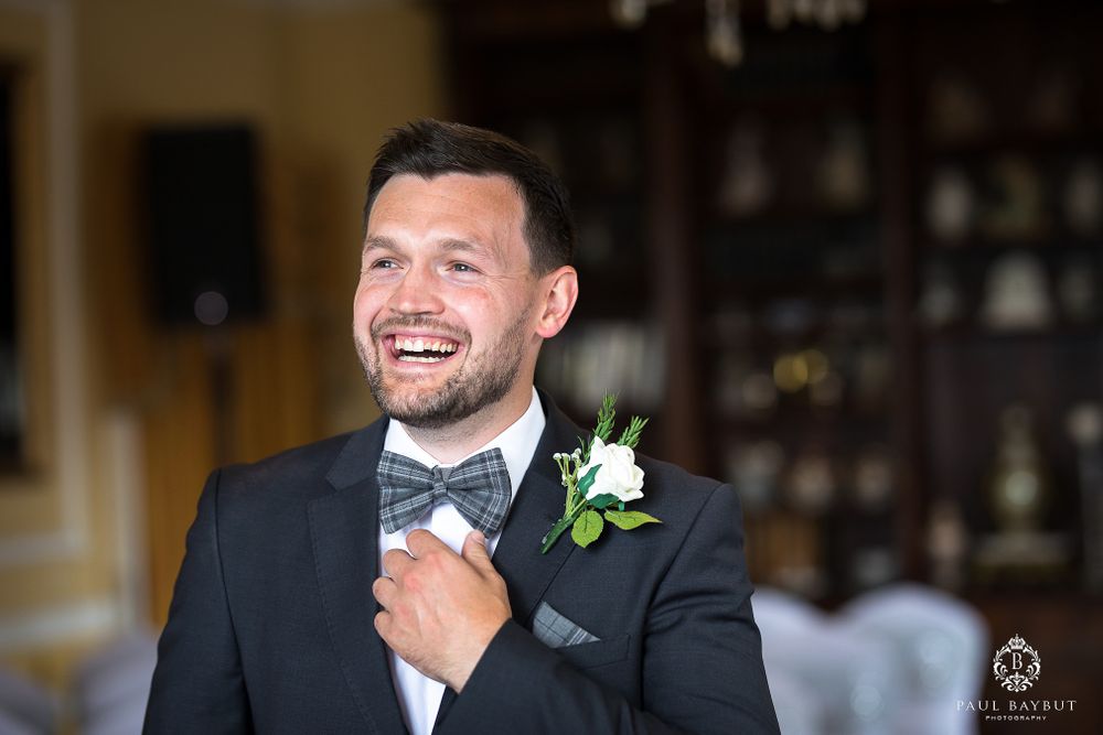 Groom adjusts his bowtie while wearing a classic black tuxedo with white boutonniere.