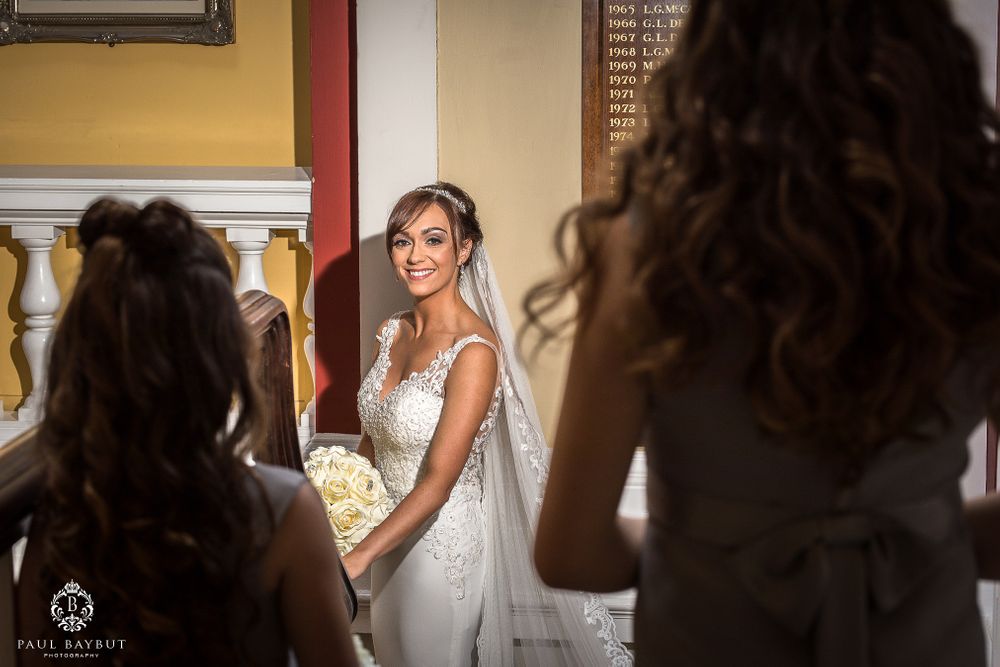 Bride in white lace gown poses for photos while holding a cream-colored bouquet.