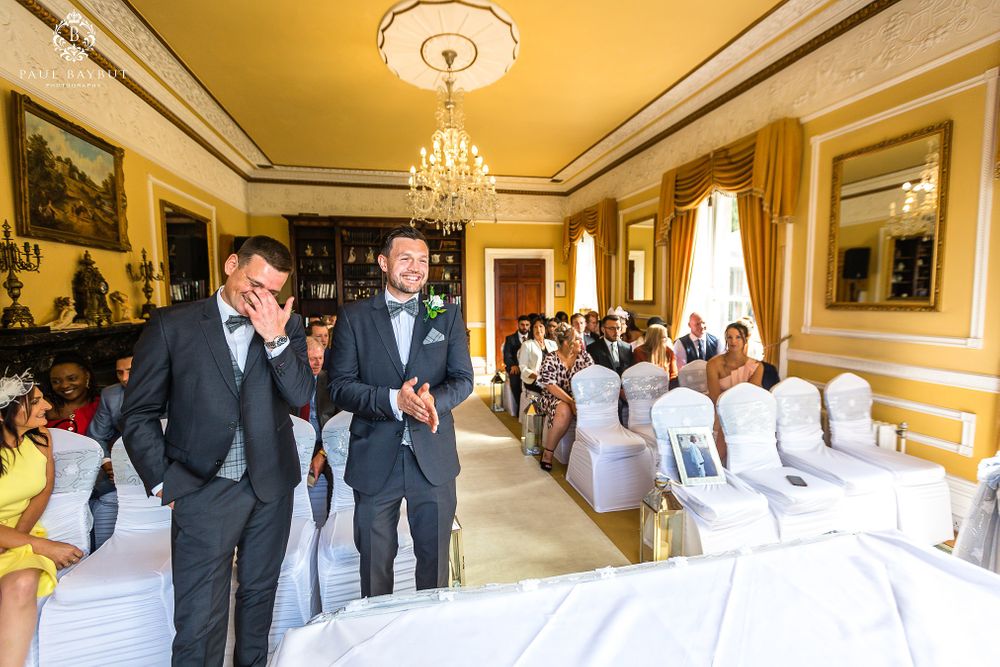 Wedding ceremony setup in yellow-walled room with elegant chandelier and white-covered chairs.