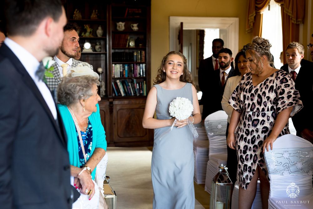 Wedding guests gather in an elegant room with chandelier and wooden shelving during an intimate ceremony.