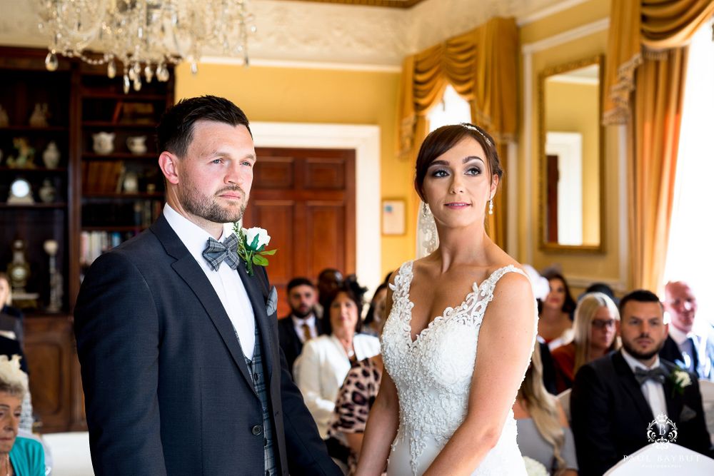 Bride and groom stand together during their wedding ceremony in an elegant room with yellow walls and crystal chandelier.