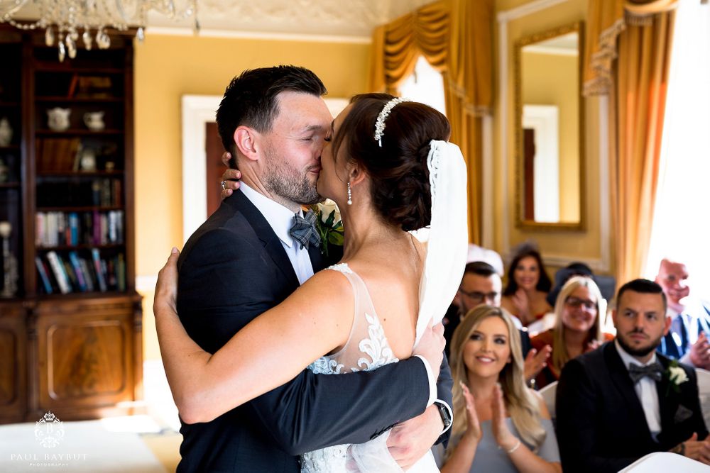 Newlyweds share their first dance in an ornate room with onlooking guests.