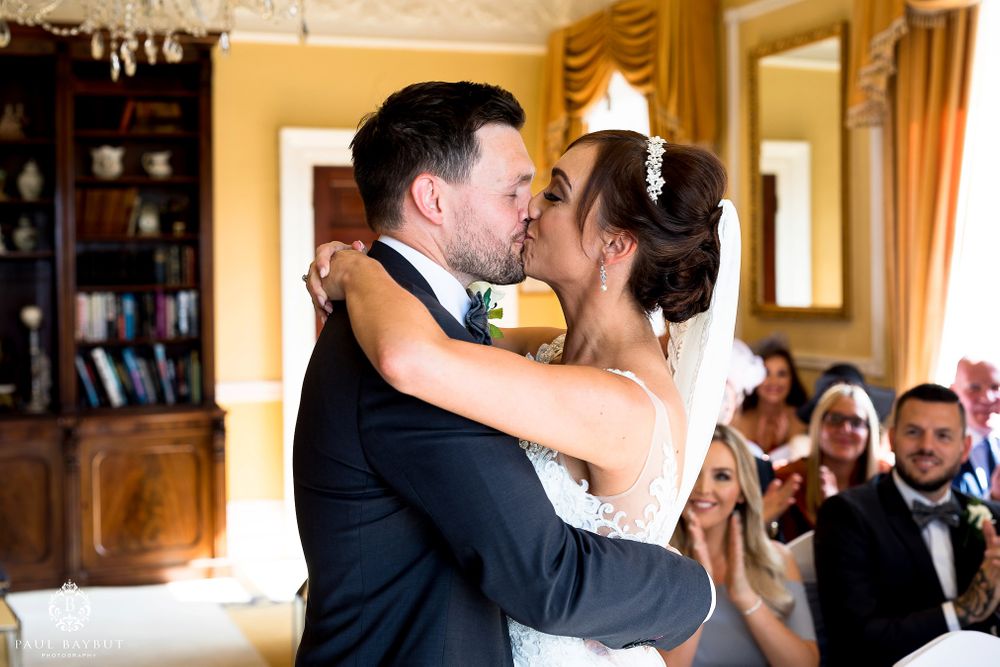 Couple shares romantic first kiss during wedding ceremony while guests watch.