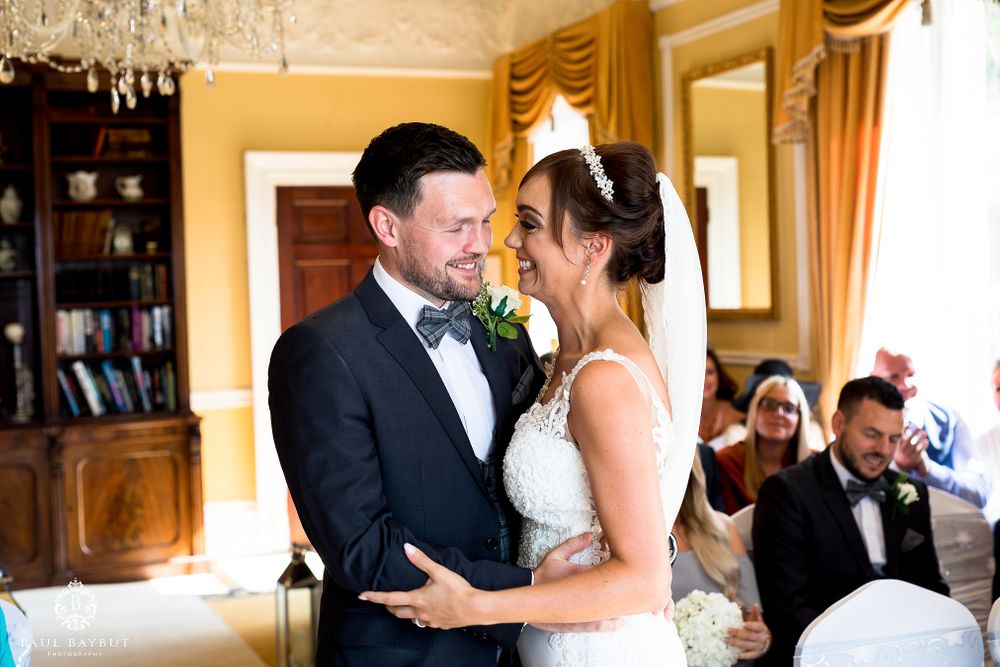 Couple shares intimate moment during wedding ceremony in elegant yellow room.
