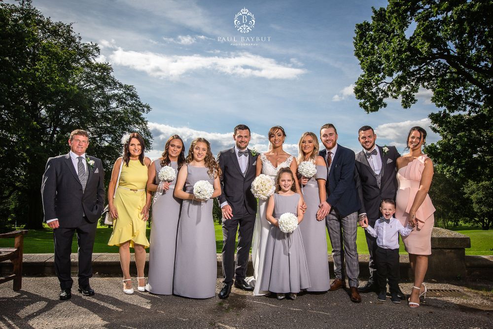 Wedding party poses for formal group photo outdoors on a sunny day.