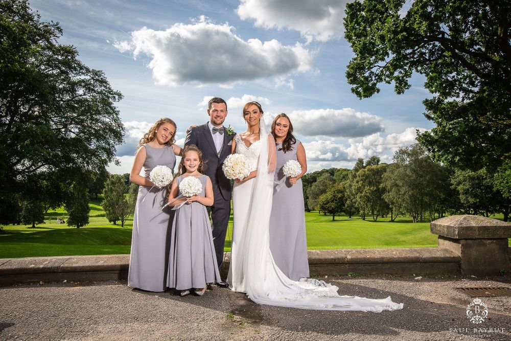 Bridal party poses together outdoors with scenic cloudy sky background.
