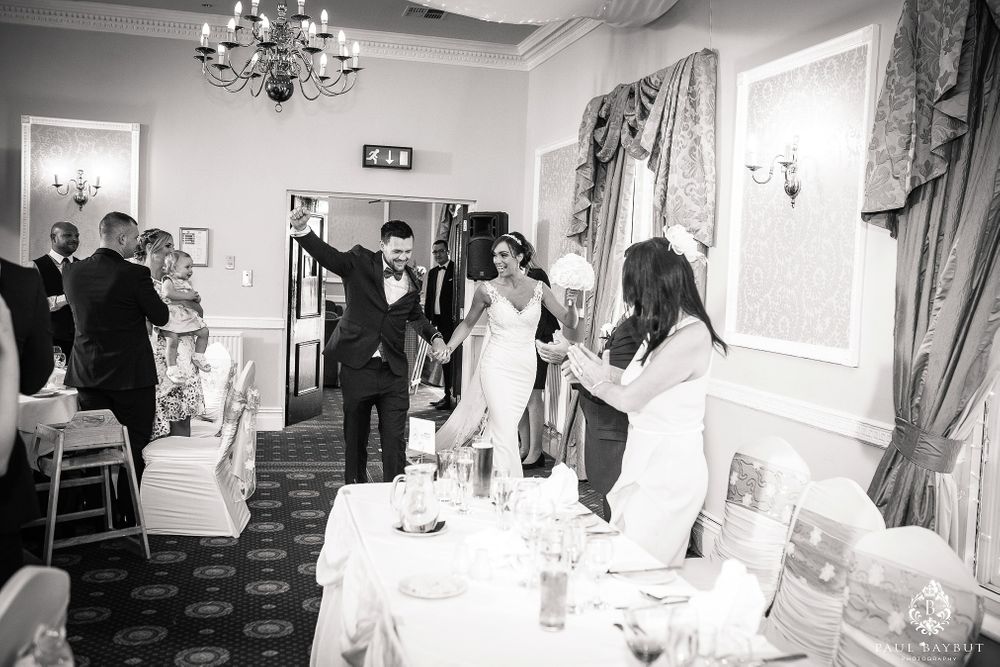 Black and white photo of wedding guests mingling in an elegant banquet hall with chandeliers.