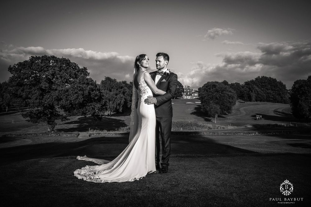 Black and white portrait of a wedding couple standing on a rolling hillside.