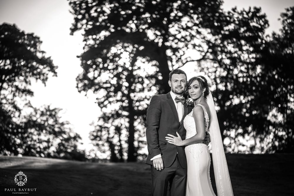 Dramatic black and white portrait of newlyweds embracing on a hilltop.