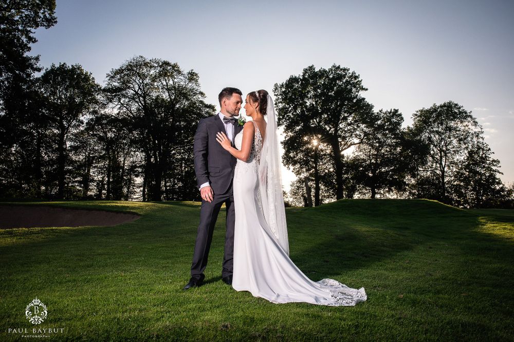Elegant wedding couple poses on rolling green hills at dusk.