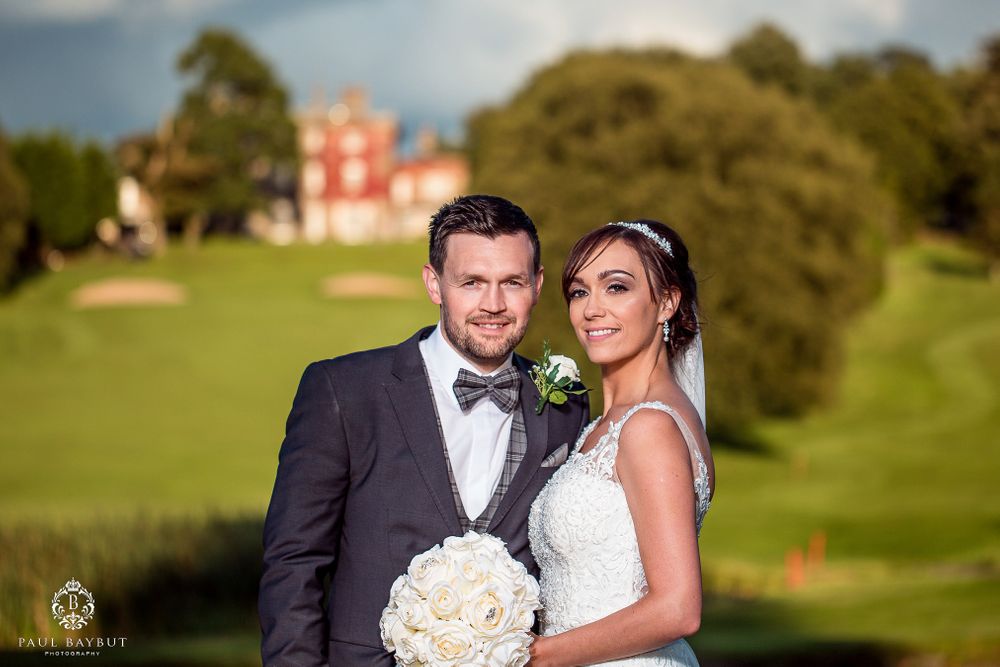 Wedding portrait with elegant couple against backdrop of historic manor house.