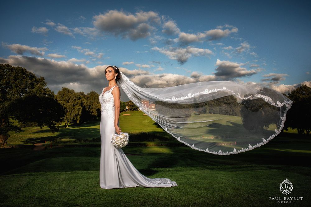 Bride with flowing cathedral veil poses on hillside as wind catches her dramatic long train.