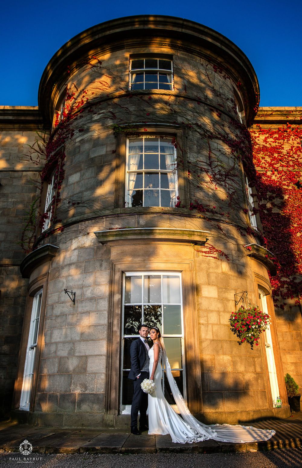 Couple poses in front of historic stone turret building with dramatic evening lighting.